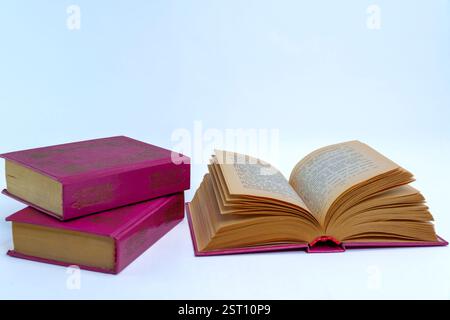 Un livre ouvert vintage à couverture rigide avec des pages jaunies à côté d'une pile de deux livres fermés sur un fond neutre. La répresentine du concept de littérature classique Banque D'Images