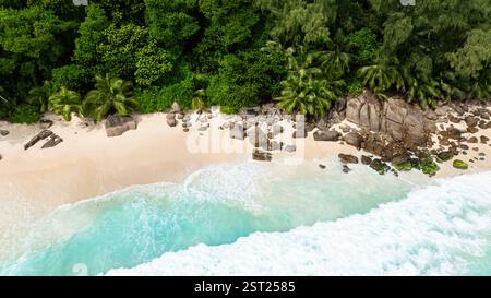 Les eaux turquoises de l'océan se baignent sur les rochers le long d'une plage tropicale luxuriante. Seychelles, Mahé. Anse intendance. Banque D'Images