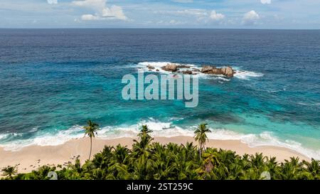 Rochers dispersés dans l'eau turquoise près de la plage avec des vagues se brisant sur le rivage. Anse Boileau. Seychelles, Mahé. Banque D'Images