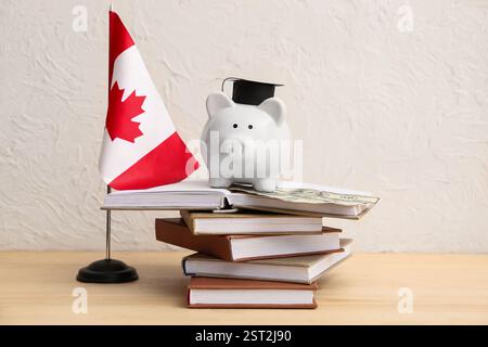 Tirelire avec de l'argent, des livres et le drapeau canadien sur la table près du mur lumineux. Concept de prêt étudiant Banque D'Images