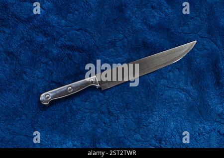 Couteau en acier placé sur fond de tissu texturé bleu profond Banque D'Images