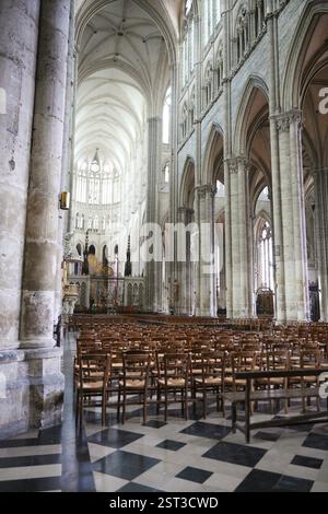 Élégant intérieur gothique de la cathédrale présentant des rangées de chaises en bois, des colonnes imposantes, des arches pointues et des vitraux complexes. Banque D'Images