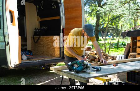 Menuisier utilisant un ruban à mesurer sur une planche de bois près de sa camionnette, se préparant à le couper avec une scie circulaire Banque D'Images