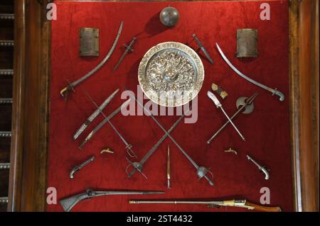Collection d'armes anciennes exposée sur velours rouge vif à Sintra, Portugal. Un éventail captivant d'épées, de poignards et de pistolets. Aperçu du Banque D'Images