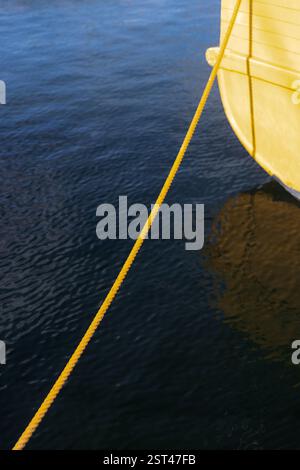 Gros plan corde d'amarrage jaune fixant un bateau en bois sur l'eau bleue Banque D'Images
