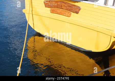 Vieux bateau en bois jaune avec signe en bois reflétant sur l'eau bleue Banque D'Images