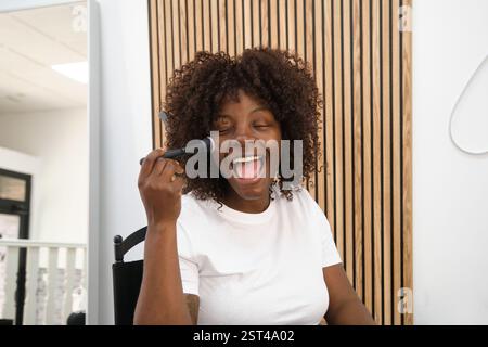 Femme joyeuse appliquant le maquillage avec le pinceau et les yeux fermés Banque D'Images