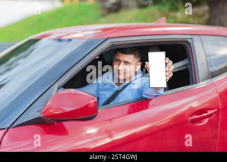 Conducteur heureux montrant l'écran du téléphone portable. Conducteur montrant un écran de téléphone cellulaire vierge à l'extérieur Banque D'Images