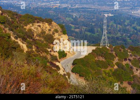 Cycliste sur une route sinueuse entourée de verdure dans Griffith Park, surplombant le paysage urbain de Los Angeles au loin. Banque D'Images