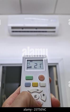 Gros plan main de l'homme tenant une télécommande au système de climatisation en appuyant sur le bouton LOW essayant de régler la température dans la pièce à un confort Banque D'Images