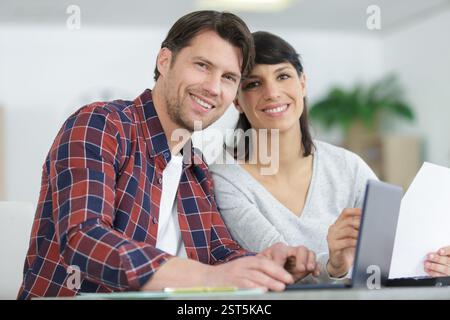 couple heureux utilisant un ordinateur portable et tenant la paperasse Banque D'Images