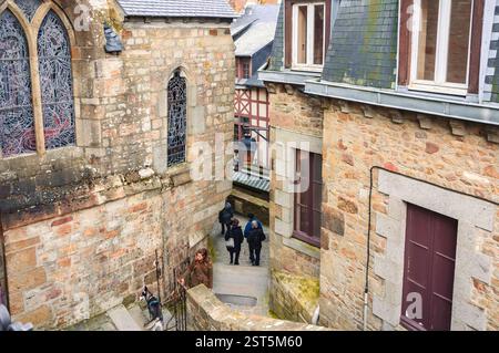 Mont Saint-Michel, France - 25 janvier 2016 : une ruelle pittoresque avec des bâtiments historiques en pierre et des touristes explorant l'architecture médiévale. Banque D'Images
