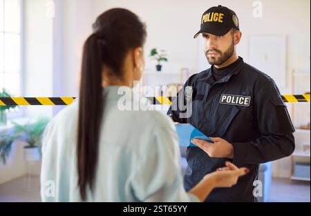 Officier de police avec bloc-notes parlant à une femme témoin à l'intérieur pendant l'enquête près de la bande de mise en garde. Banque D'Images