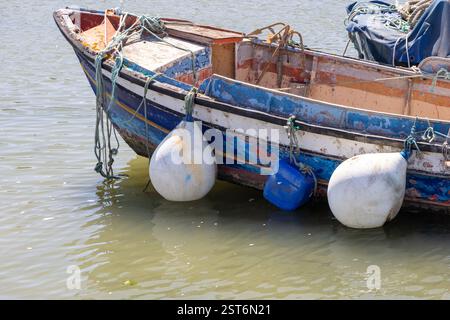 Bateau de pêche altéré avec peinture pelable, garde-boue et cordes, flottant doucement dans l'eau tranquille Banque D'Images