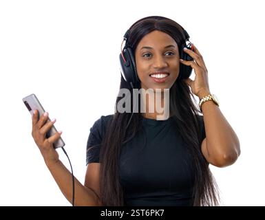 Attirante, souriante, jeune femme noire écoutant de la musique sur téléphone portable avec des écouteurs. Porter un t-shirt noir décontracté Banque D'Images