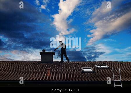 Un ramoneur nettoie la cheminée sur le toit d'une maison devant un beau ciel Banque D'Images