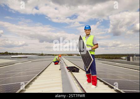 Homme positif travailleur installant des panneaux solaires sur le toit Banque D'Images