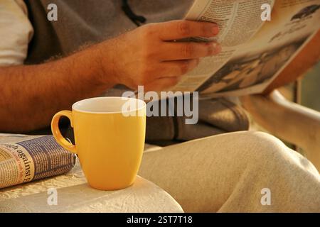 Mug jaune, mug jaune de nid de thé chaud à un homme lisant le journal MR No 646 Banque D'Images