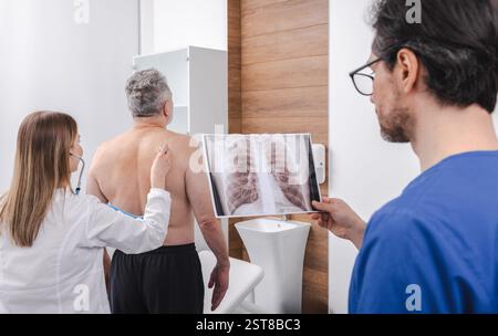 Le patient senior est examiné par un médecin pneumologue dans la clinique médicale tout en examinant les rayons X pulmonaires pour évaluer la santé et déterminer les options de traitement Banque D'Images