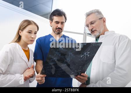 Trois professionnels de la santé, dont deux médecins et une infirmière, examinent attentivement les radiographies de la tête tout en discutant du diagnostic du patient dans une clinique Banque D'Images