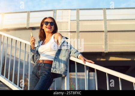 Jeune femme brune posant avec un téléphone portable à l'extérieur sur l'escalier de la ville Banque D'Images