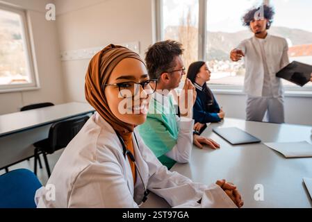 Une équipe médicale discutant lors d'une réunion dans le bureau d'une femme musulmane médecin en hijab souriant regardant la caméra. Banque D'Images