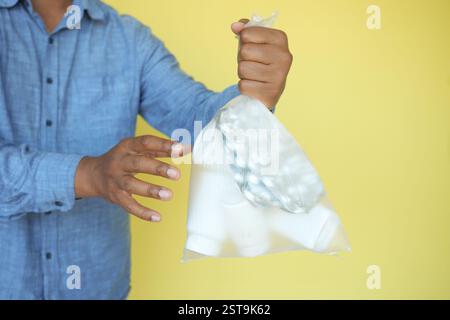 Tenir un sac de gobelets en plastique contre un mur jaune Banque D'Images