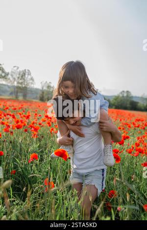 tour de piggyback de la jeune fille sur l'enfant aîné dans un champ de coquelicots Banque D'Images