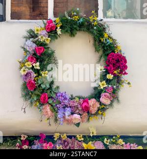 Couronne d'été confectionnée à partir de fleurs de soie dans des teintes roses, mauves et jaunes ornant le mur extérieur blanc d'une maison. ROYAUME-UNI Banque D'Images