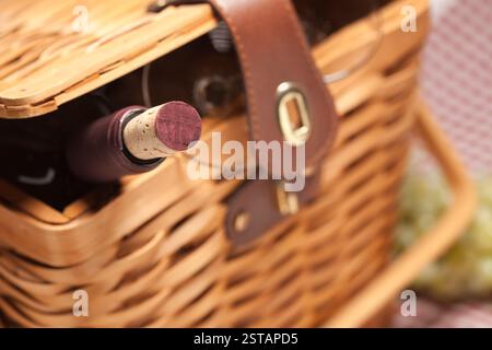 Panier pique-nique, bouteille de vin et verres vides sur une couverture Vichy. Banque D'Images