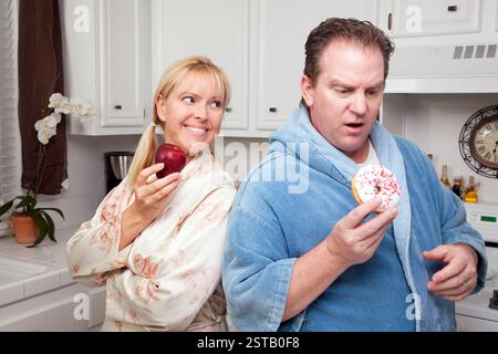 Couple in Kitchen Eating Donut et de café ou de fruits sains. Banque D'Images