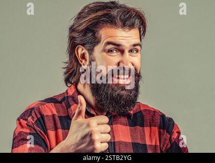 Jeune homme beau avec la barbe portant une chemise à carreaux, signe de succès faisant un geste positif avec la main, les pouces vers le haut souriant et heureux. Heureux jeune homme avec Banque D'Images