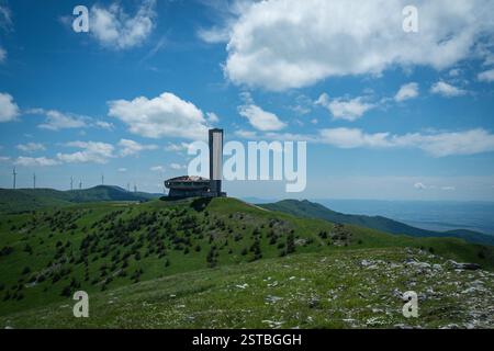 Monument isolé de Buzludzha, également connu sous le nom de vaisseau spatial, situé au sommet d'une montagne verdoyante, encadrée par un ciel bleu clair et des éoliennes Banque D'Images