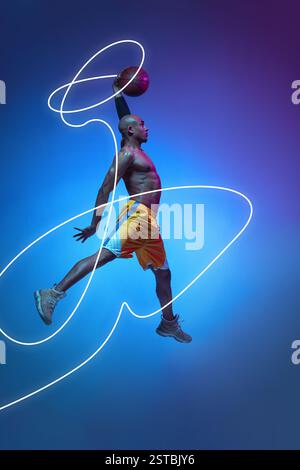Homme musclé, joueur de basket-ball dans le ballon de dunking en plein air, saut puissant capturé avec une traînée lumineuse au néon tourbillonnant autour sur fond bleu dégradé Banque D'Images