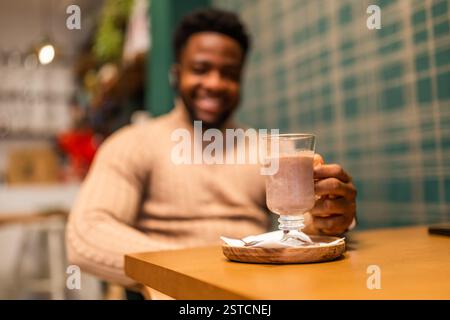 Jeune homme noir appréciant le chocolat chaud dans la barre. Focus sélectif sur le verre avec du chocolat chaud. Banque D'Images