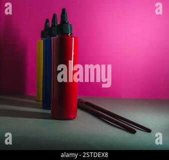 Bouteilles de peinture colorée alignées sur un fond rose vif avec des pinceaux à côté d'eux Banque D'Images