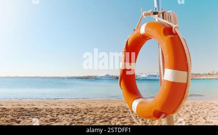 Cercle de bouées de sauvetage. Vue panoramique de bouée de sauvetage rouge et blanche sur le poteau sur la plage de bord de mer. Paysage de paysage de la rive de l'océan de mer le jour ensoleillé. Dispositif de sauvetage en eau Banque D'Images