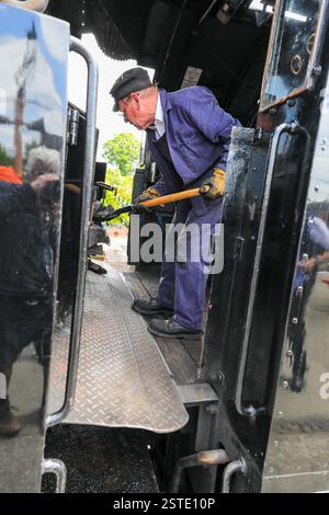 Un pompier âgé sur la plaque de pied attisant le feu sur une machine à vapeur ou une locomotive à vapeur, Angleterre, Royaume-Uni Banque D'Images