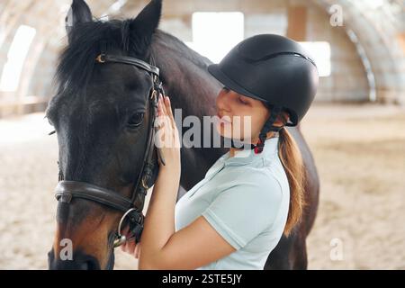 Préparation de l'équipement. Une jeune femme en tenue de jockey est avec un cheval sur une écurie. Banque D'Images