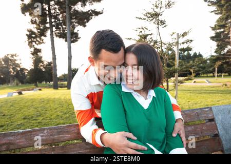 Un jeune couple latino affectueux apprécie une étreinte chaleureuse sur un banc de parc, se prélasser dans la lueur du coucher du soleil Banque D'Images