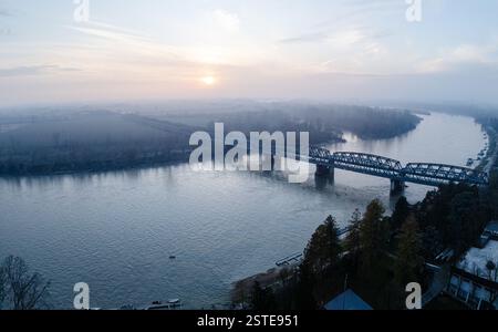 Cremona, Italie - 9 février 2025 coucher de soleil d'hiver vue aérienne du fleuve po avec pont de chemin de fer et brouillard léger en Lombardie, Italie Banque D'Images