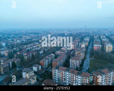 Cremona, Italie - 9 février 2025 vue aérienne capturant le quartier résidentiel de la ville avec le clocher Torrazzo qui s'élève à travers la brume hivernale au coucher du soleil Banque D'Images