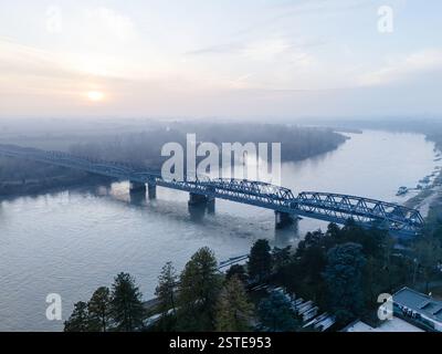 Cremona, Italie - 9 février 2025 vue aérienne du fleuve Pô avec un pont qui le traverse lors d'un coucher de soleil brumeux en Lombardie, Italie Banque D'Images
