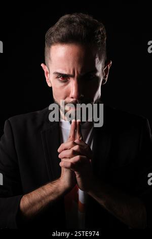 Un homme d'apparence sévère dans un costume sombre et des lentilles de contact rouges avec un visage mi-éclairé enveloppé de fumée sur un fond noir, exsudant mystère et drame Banque D'Images