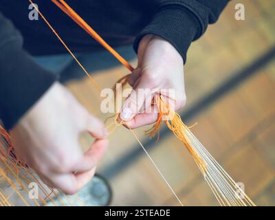 Gros plan de mains gérant habilement les fils orange tout en travaillant des machines dans une chaîne de production de fils, représentant la fabrication textile industrielle Banque D'Images