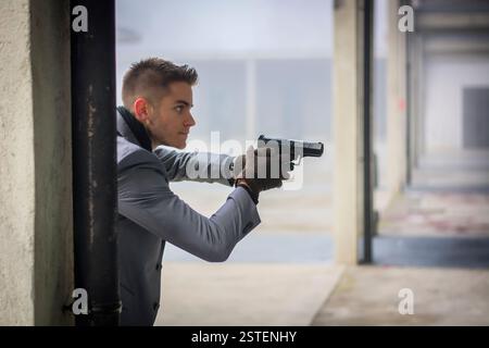 Bien habillé beau jeune détective ou policier ou gangster debout dans un environnement urbain tenant un pistolet avec un déterminé e Banque D'Images