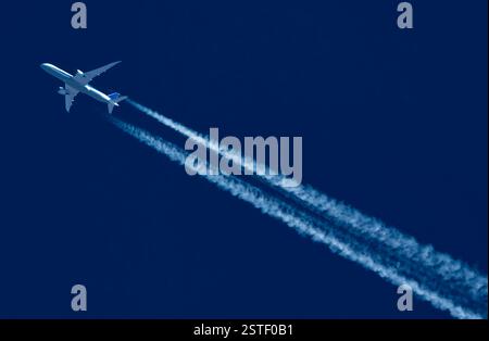 L'avion de ligne commercial voyage à travers le ciel avec des traînées de vapeur jumelles contre un ciel bleu foncé. Banque D'Images