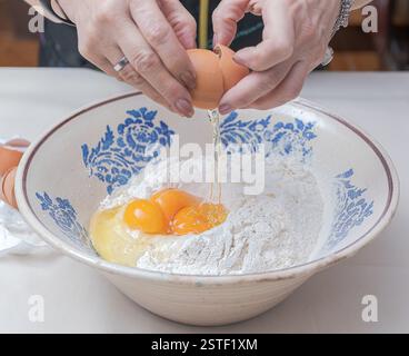 Craquer un œuf avec vos mains et le verser sur la farine dans un bol en céramique. Banque D'Images