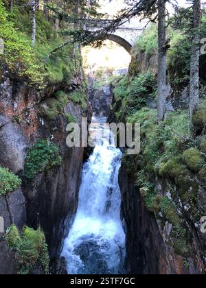 Une magnifique gorge remplie d'eau ruisselante coule à travers des formations rocheuses, baignées de soleil, tandis qu'un vieux pont de pierre vole gracieusement au-dessus de la tête Banque D'Images