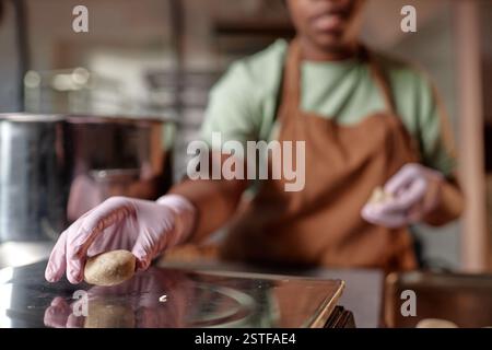 Gros plan sur la main de chef pâtissier féminin méconnaissable travaillant dans des gants en latex écaillant la pâte de forme ronde tout en faisant des petits pains feuilletés dans la cuisine de boulangerie, espace de copie Banque D'Images